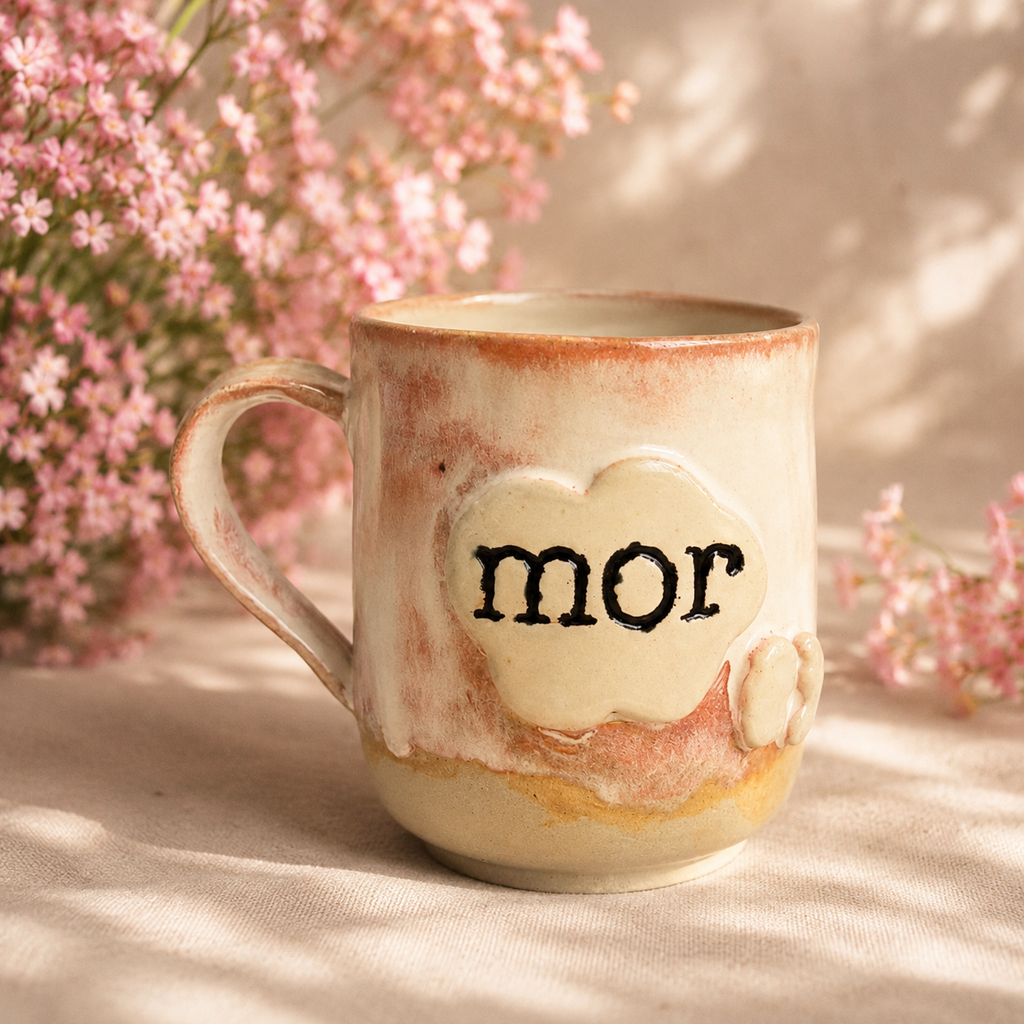 Detalje af den håndlavede kop med teksten “mor” og små babyfødder i keramik.