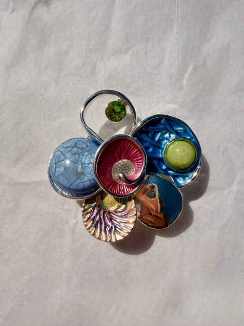 Farverig kunstbroche med blå detaljer og sølvfinish