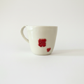 Håndlavet hvidt porcelænskrus med røde hjertedetaljer i enkelt lyst studiemiljø. Elegant og romantisk design til kaffe og te.
