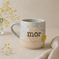 Håndlavet stentøjskop med teksten “mor” og gul blomsterdetalje i bløde lyse nuancer.