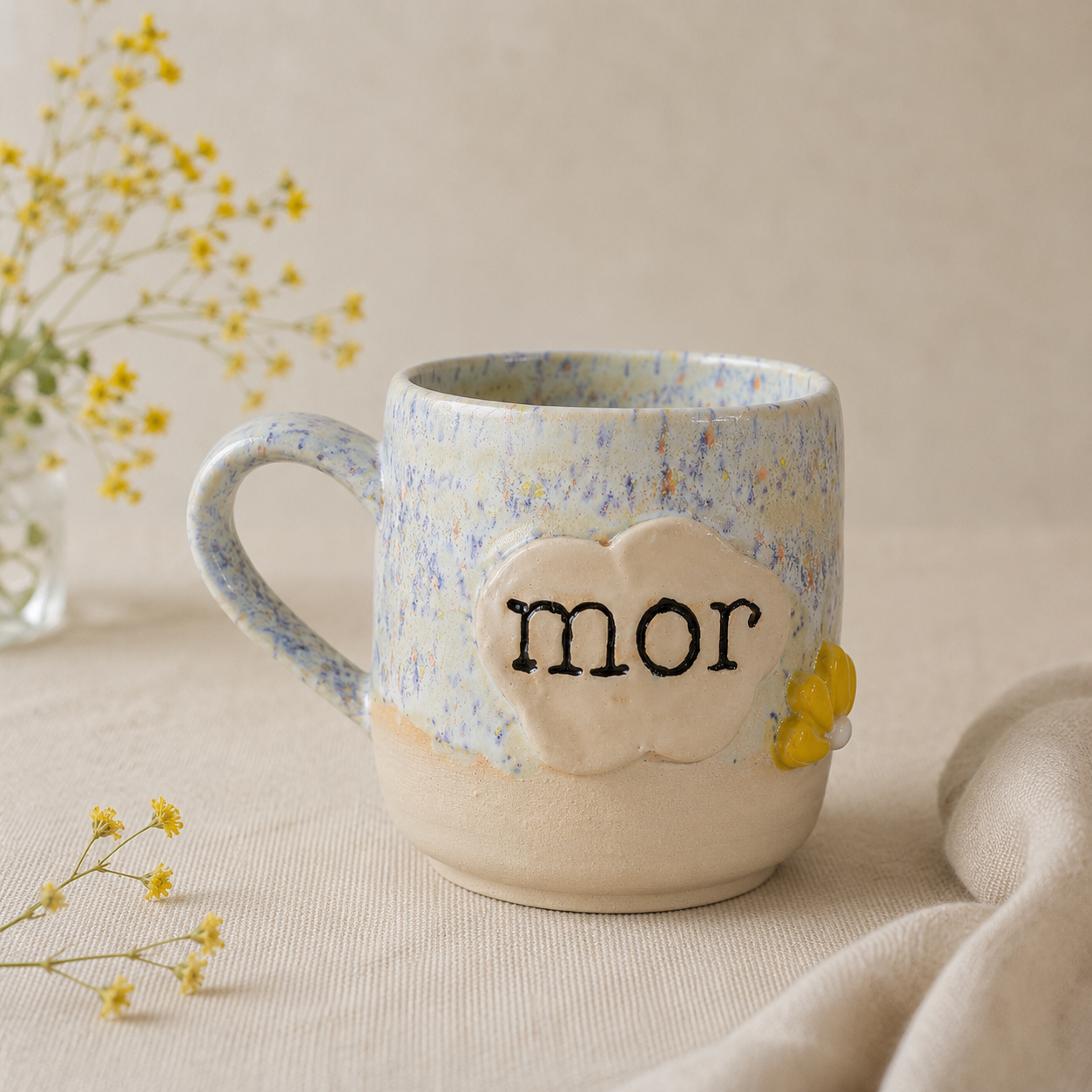Håndlavet stentøjskop med teksten “mor” og gul blomsterdetalje i bløde lyse nuancer.