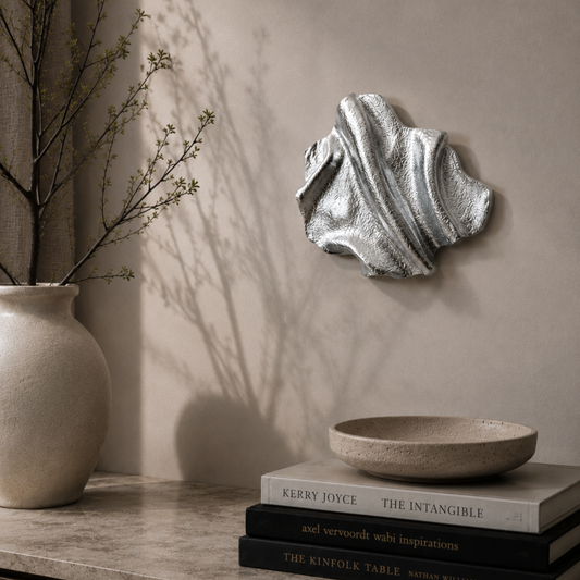 Håndlavet vægkunst i chromefarvet aluminium med organiske, bølgende former og en spejlblank overflade. Værket er fotograferet i et lyst, minimalistisk interiør, hvor de reflekterende detaljer fremhæves af det naturlige lys.
