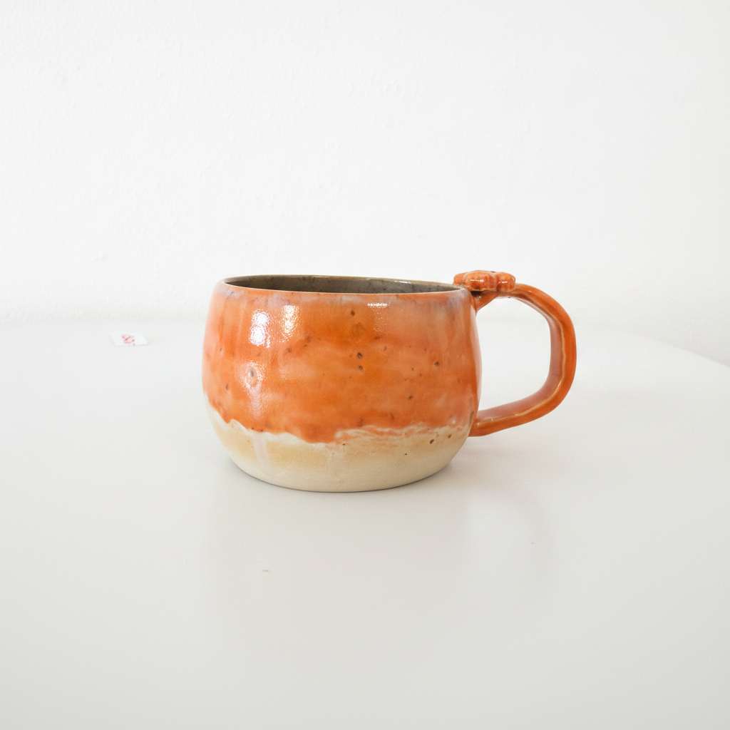 Unika keramikkop med levende orange glasur og håndformet hank set fra siden.